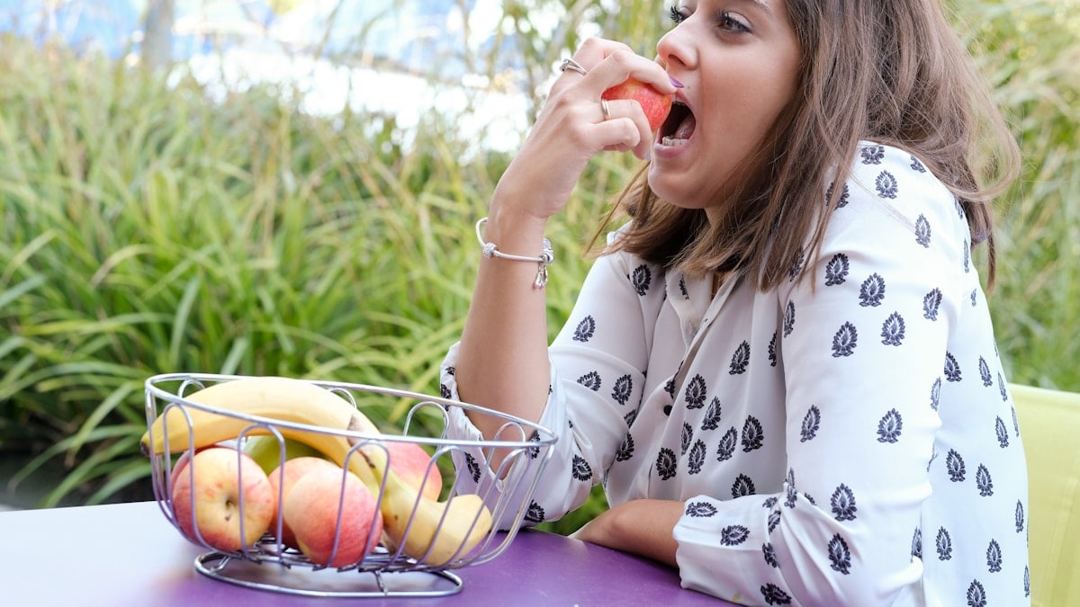 a woman sitting at a table eating an apple