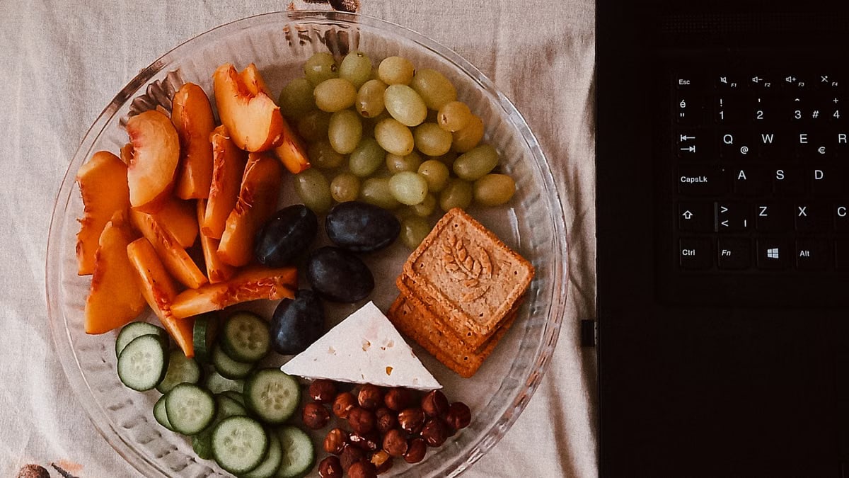 A delightful snack plate with fruits, cheese, and a laptop for a healthy lifestyle.